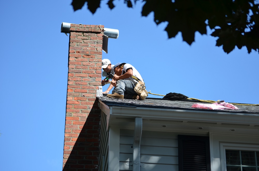 Two O'lyn Roofing contractors on top of a house working on repairing a roof leak near the chimney.