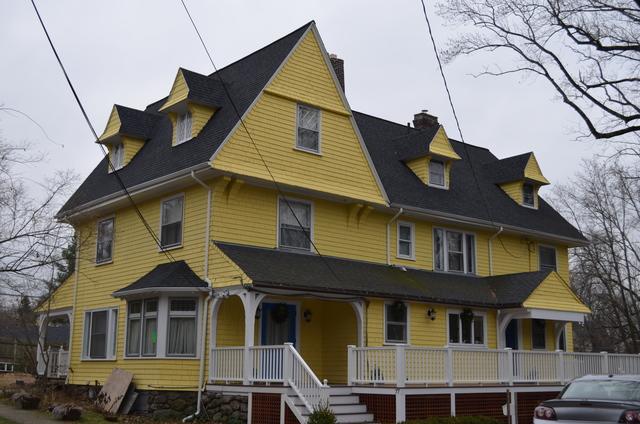 Three story yellow house with a white wrap around porch.