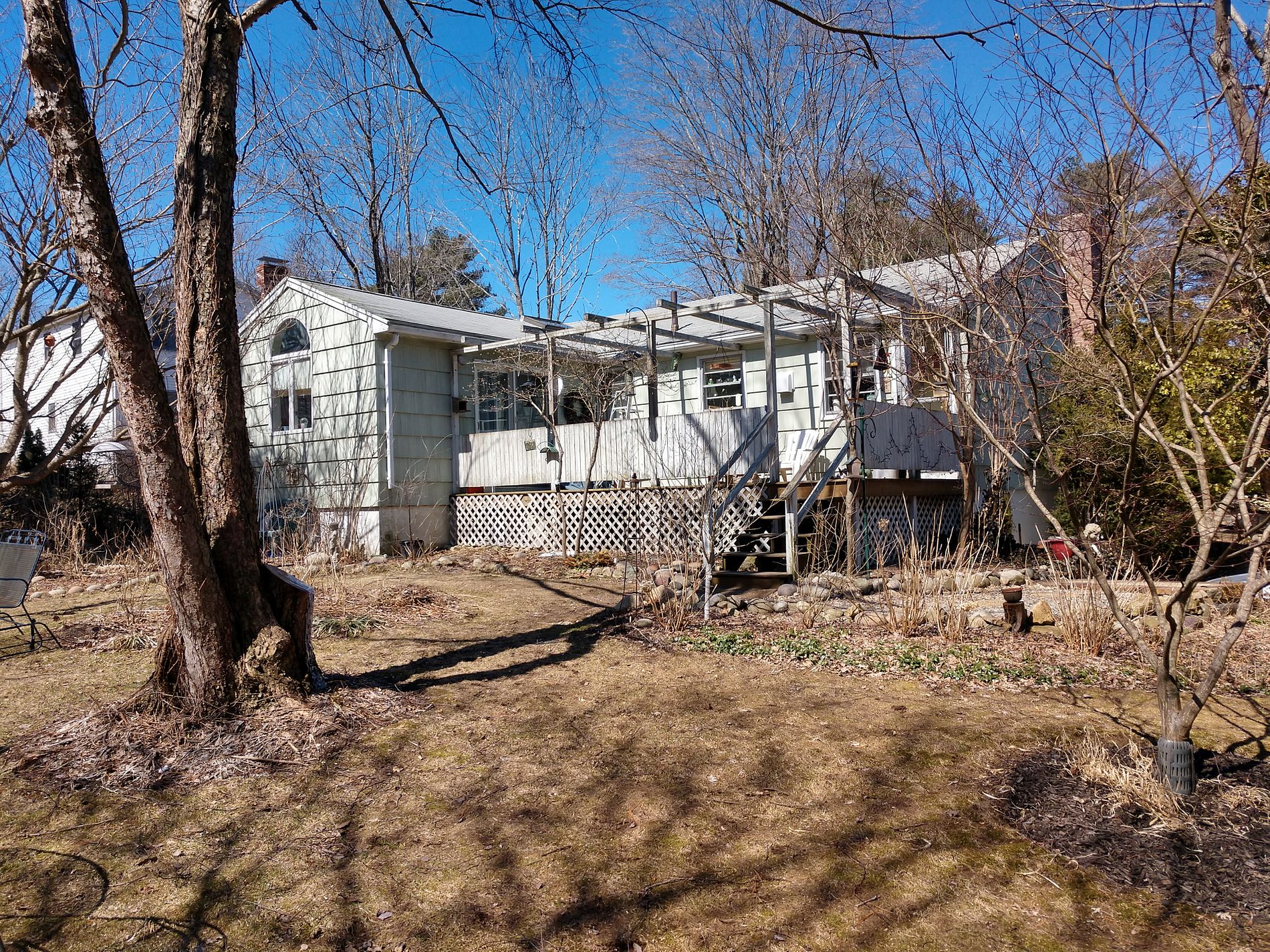 Backyard view of an older single-story home with a light-colored metal roof, a raised wooden deck, and a lattice skirting