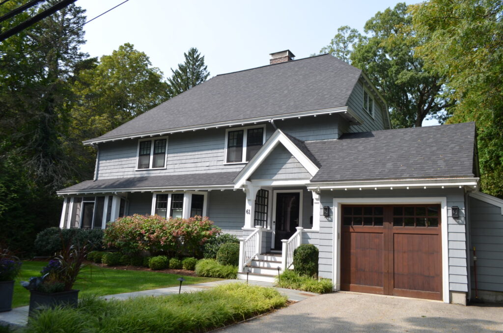 Elegant two-story house with gray siding and a dark gray shingle roof, featuring a landscaped front yard, white trim, and wooden garage door