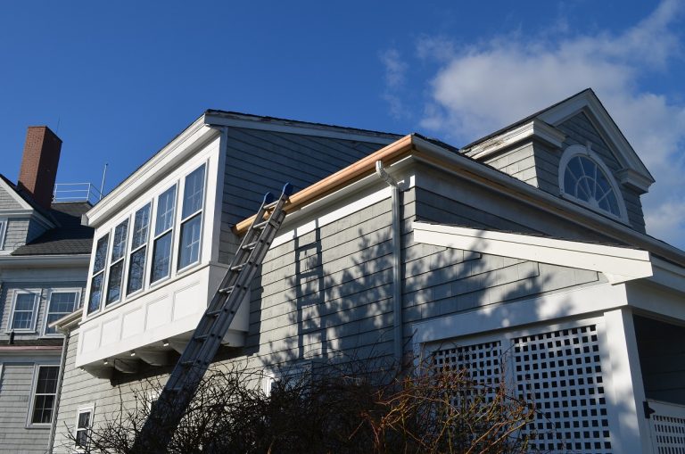  A two story gray home with a crew installing new wood gutters. 
