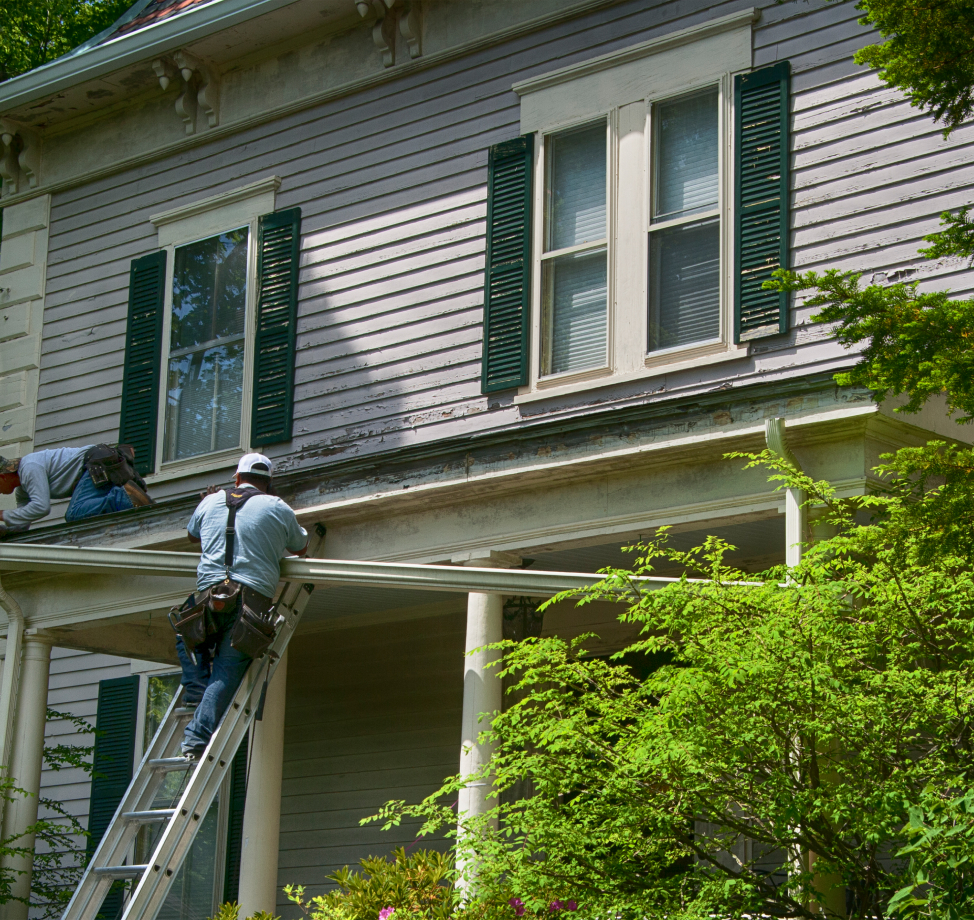 Roofers repairing porch roof on older two-story home with green shutters