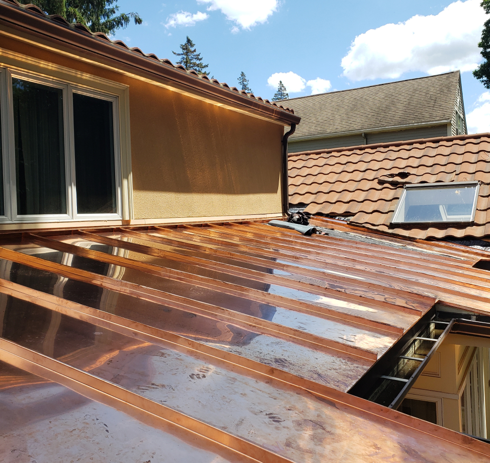 New copper roof installed next to tile roof with skylight.