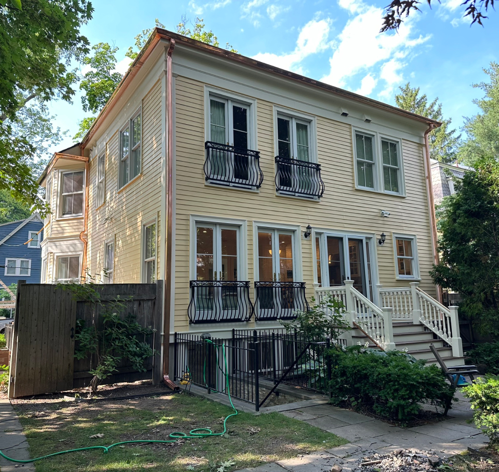 Rear view of yellow house with French doors and black iron balconies.