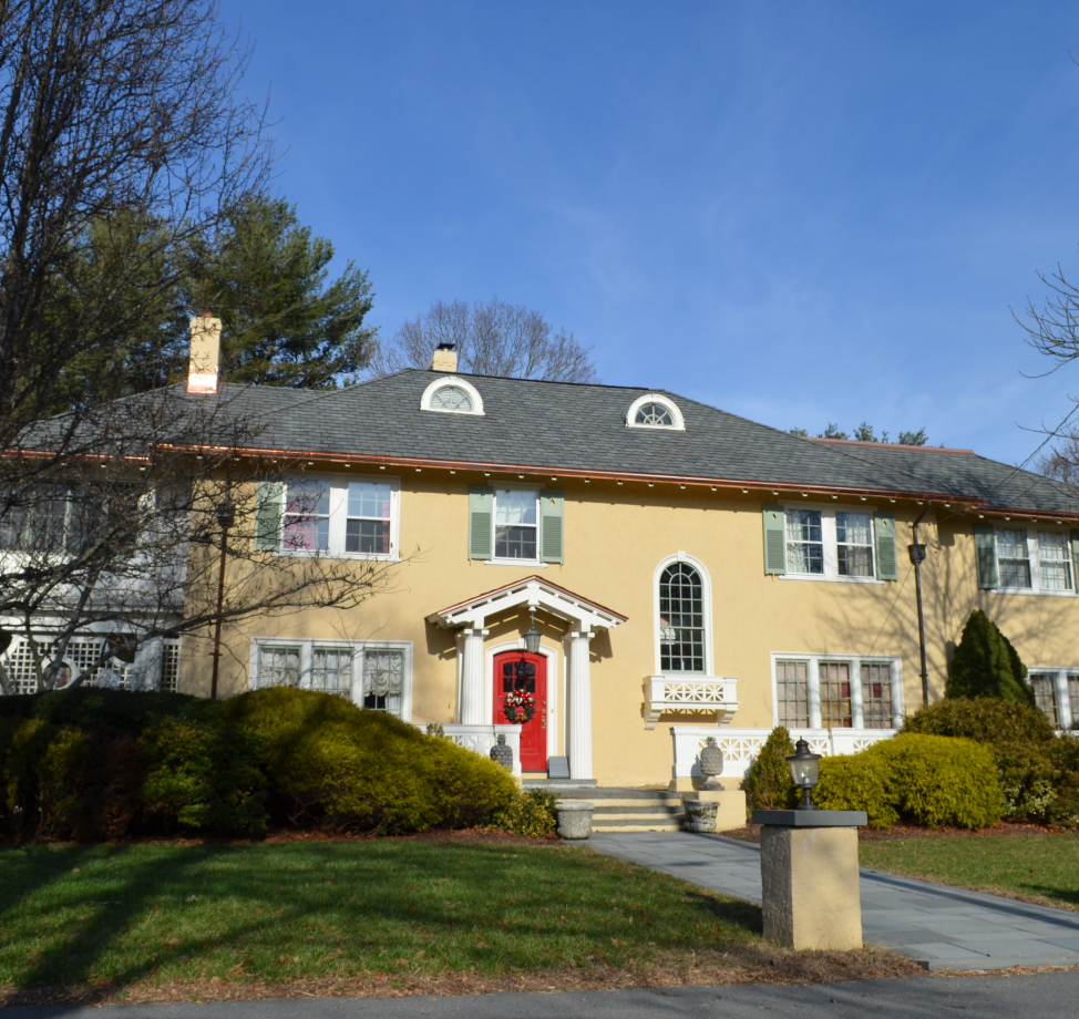 Stucco colonial home with red door, arched windows, and slate roof.