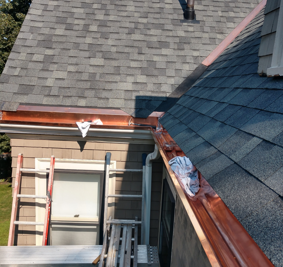 New copper gutter installation on shingled roof with ladders and scaffolding below.