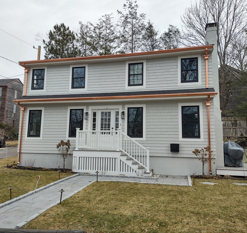 Gray two-story house with black windows and new copper gutters and downspouts.
