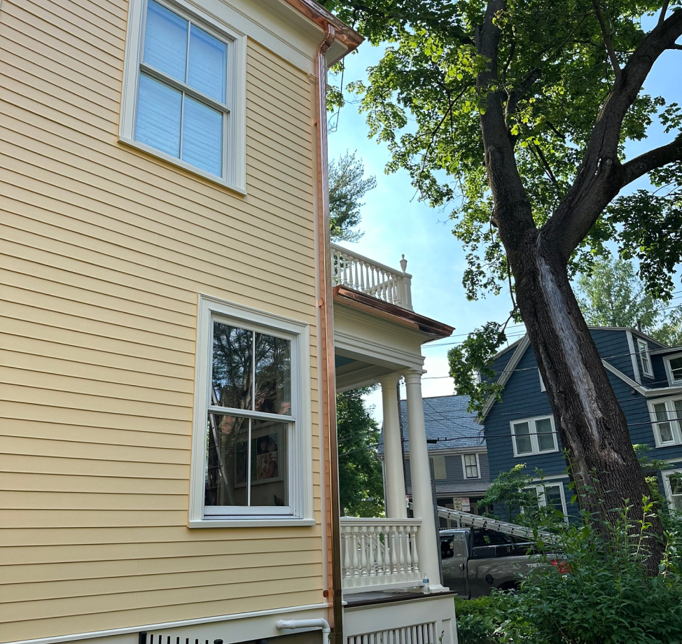 Side of yellow house with new copper downspout and front porch columns.