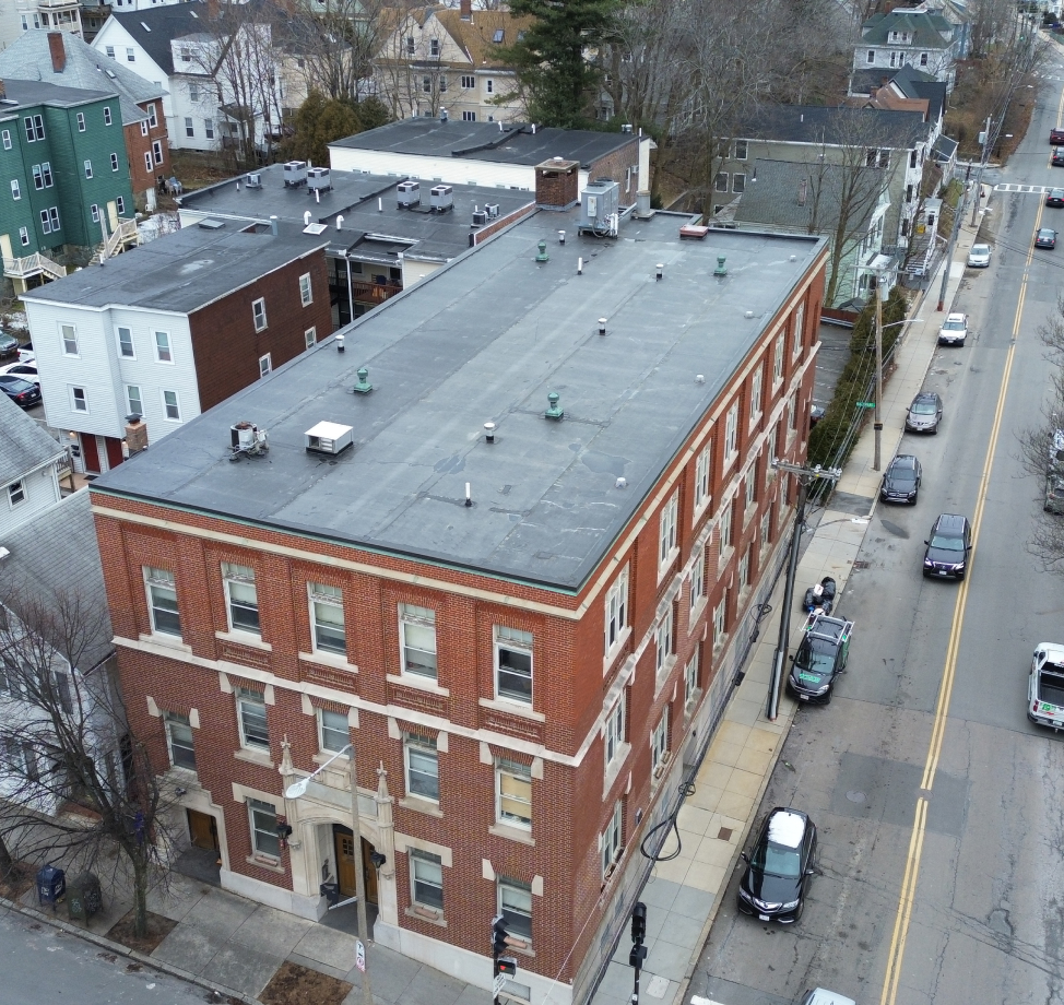 Aerial view of flat-roofed brick apartment building on a city street corner.