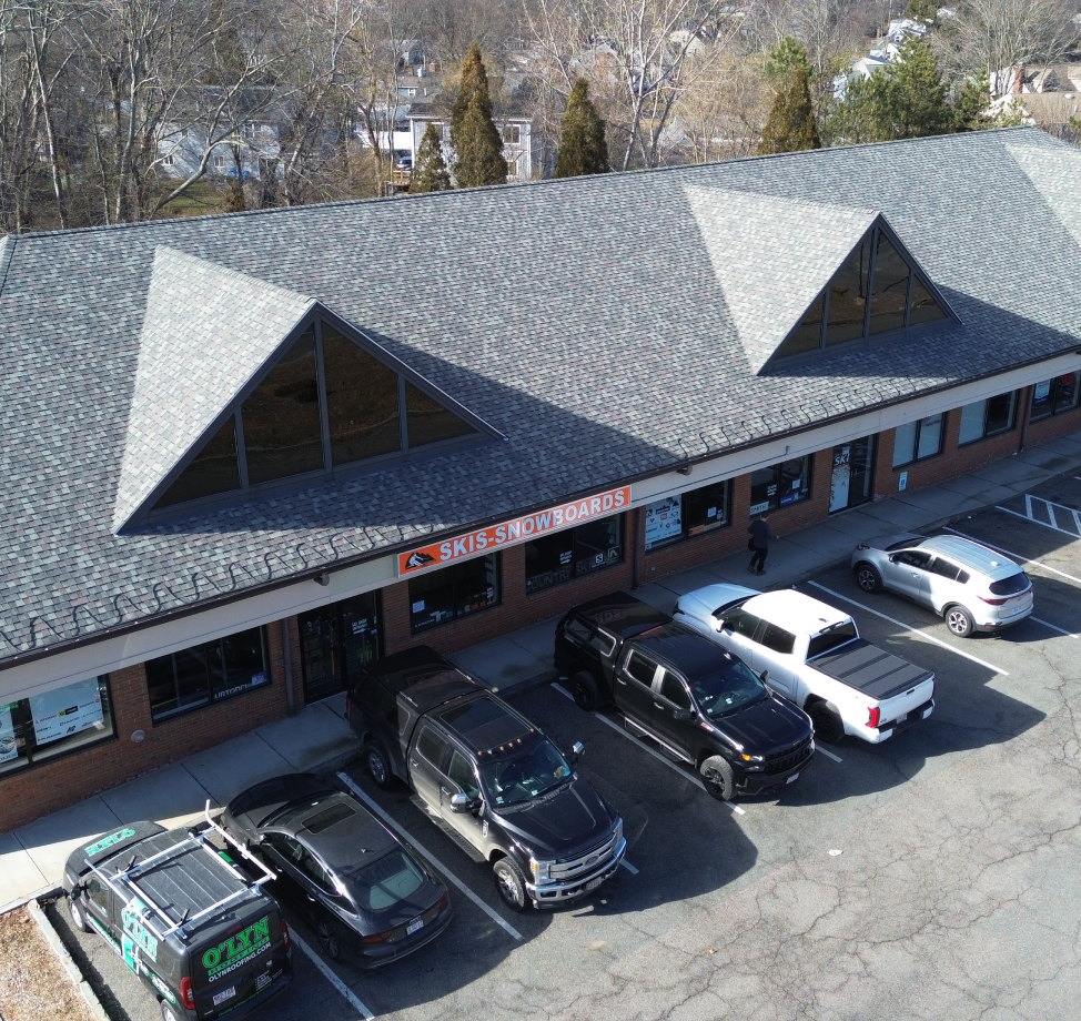 Retail plaza with new shingle roof and O’Lyn Roofing van parked in front.