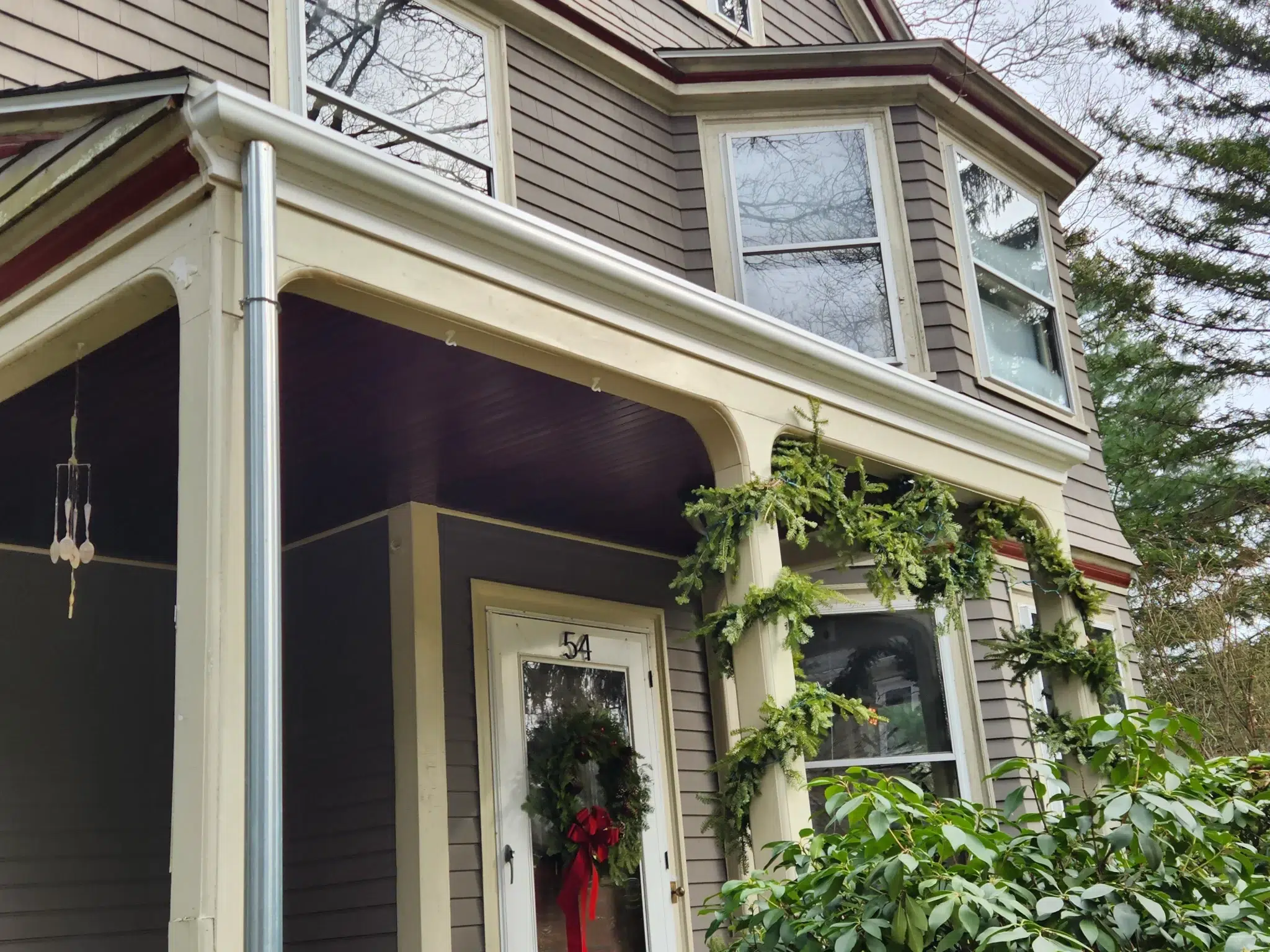 Fiberglass gutters on brown Victorian style house with green garland wrapped around the front porch columns.