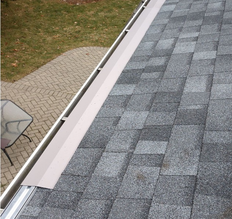 Close-up view of gray asphalt shingles and newly installed drip edge above a metal gutter system.