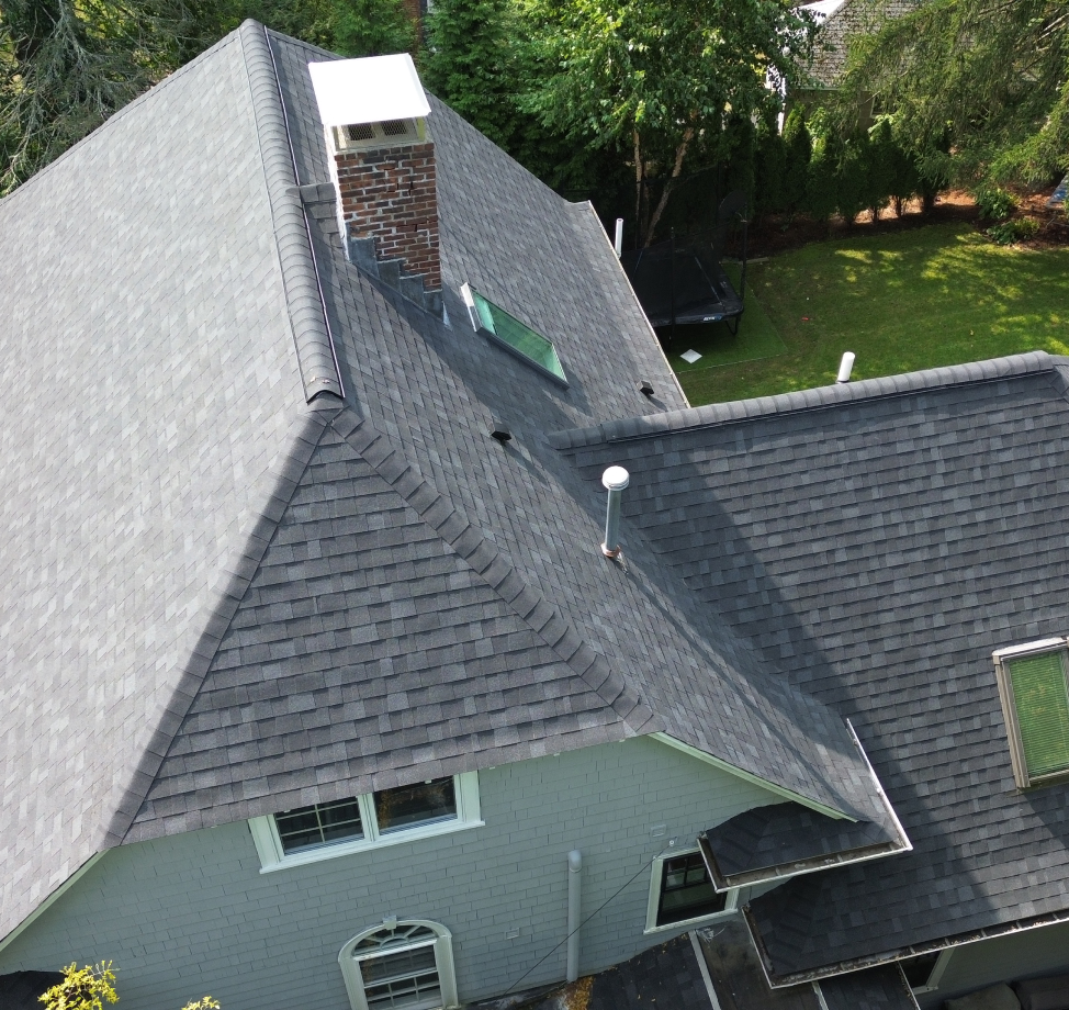Steeply pitched gray shingle roof with skylight and brick chimney on a two-story gray painted home.