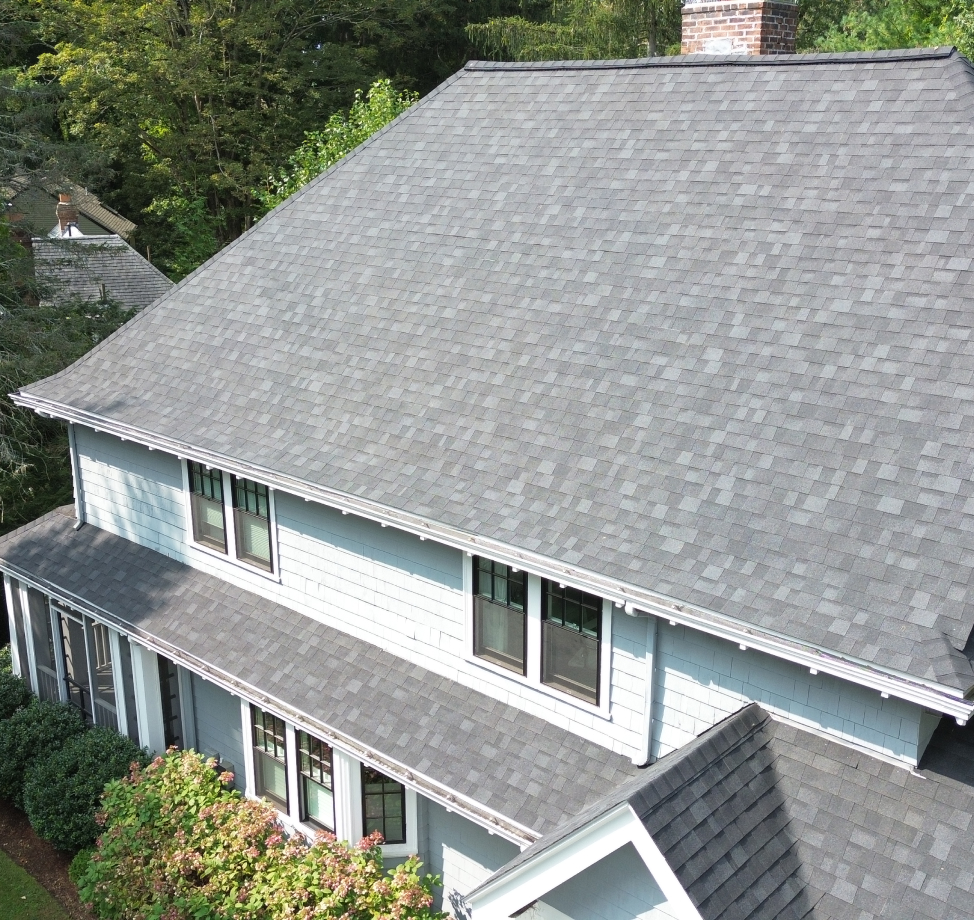 Angled view of light blue house with large gray shingle roof and brick chimney.