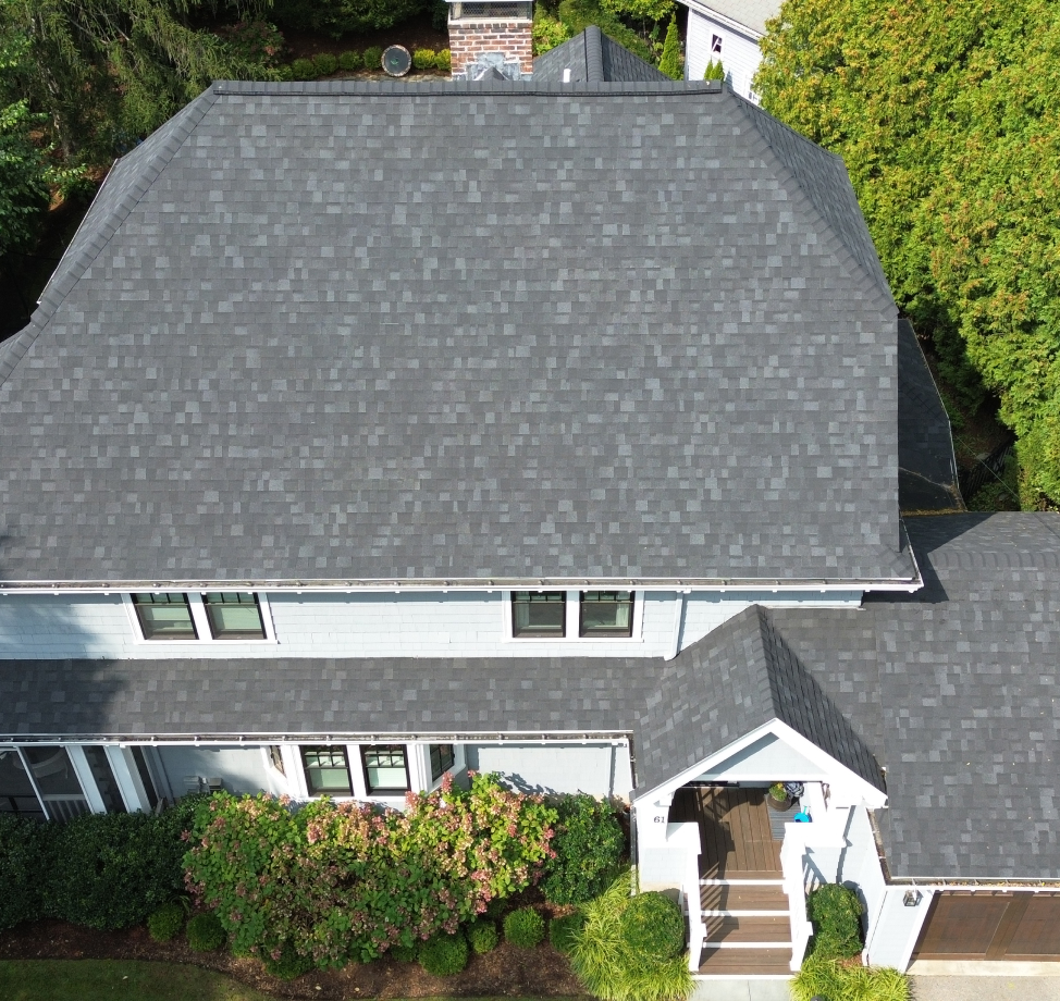 Aerial view of house with dark gray asphalt shingle roof and landscaped front yard.