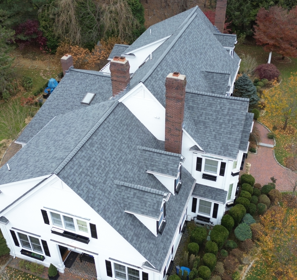 Large white colonial home with multiple chimneys and dormers, featuring a new architectural shingle roof.
