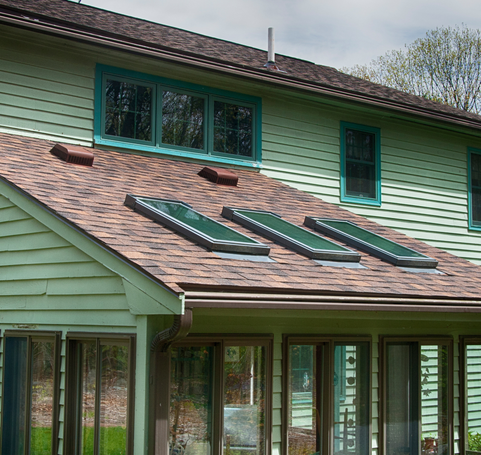 House with three skylights on shingled roof and green siding.