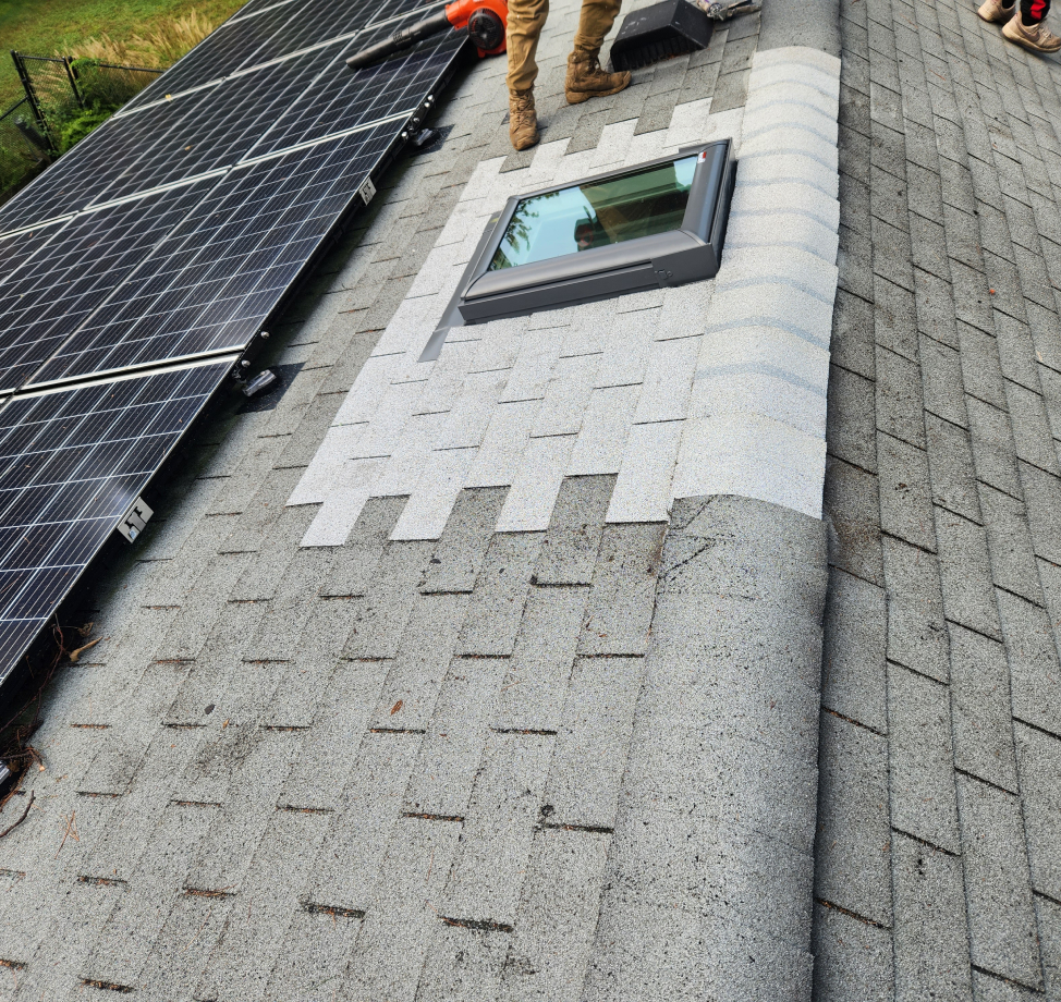 Roof repair around skylight on asphalt shingle roof with nearby solar panels