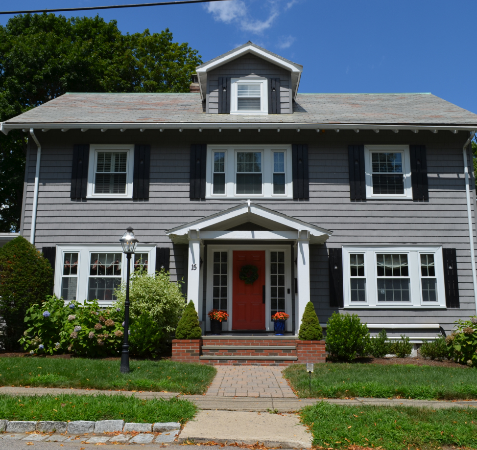 Gray Colonial-style house with red door, black shutters, and gable dormer.
