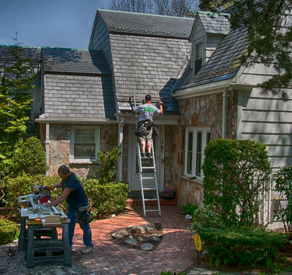 Roofers installing asphalt shingles on stone and siding home