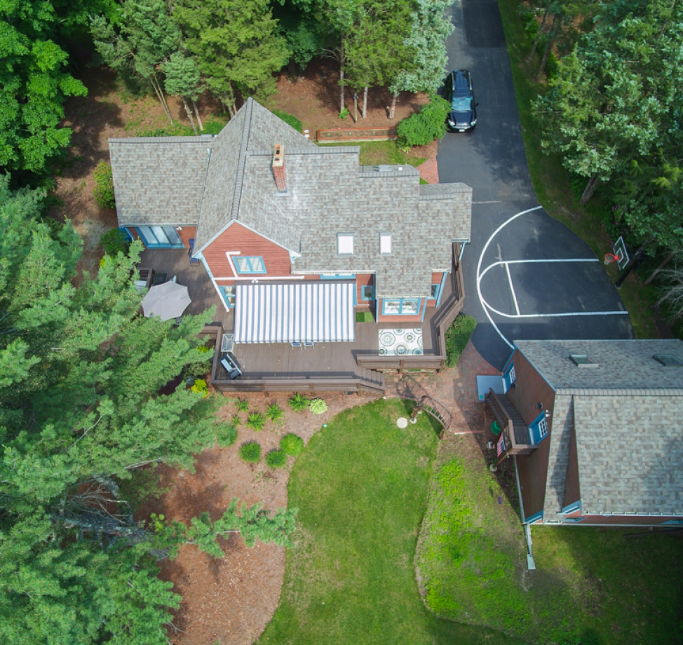 Aerial view of a red and beige home with new light gray asphalt shingle roofing and a backyard deck area